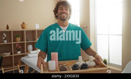 Un giovane sorridente in una sala spa con un vassoio con attrezzi per massaggi, creando un'atmosfera rilassante e terapeutica in un centro benessere Foto Stock