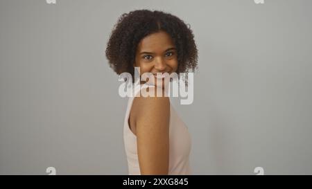 Una bella giovane donna afroamericana con i capelli ricci si posa con sicurezza su uno sfondo bianco isolato. Foto Stock