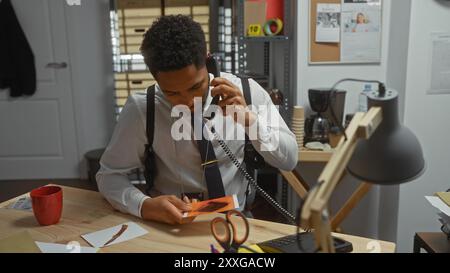 Detective afroamericano che analizza le prove mentre parla al telefono in un ufficio di polizia. Foto Stock