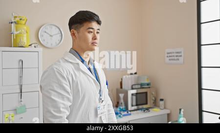 Un giovane uomo asiatico vestito da professionista sanitario si trova in un ambiente di laboratorio moderno e ben attrezzato. Foto Stock
