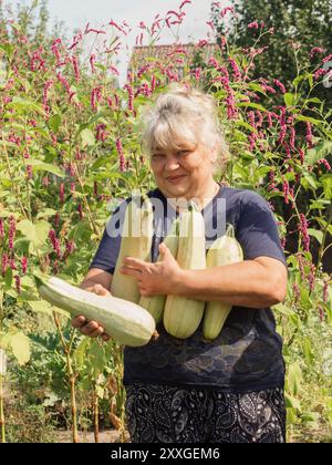Proud Harvest: Ritratto verticale di una donna Ucraina anziana che tiene zucchine appena raccolte nel Volyn Village Foto Stock