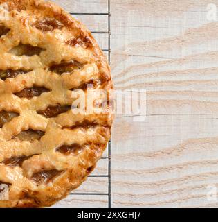 Vista dall'alto di una torta di mele natalizie appena sfornata su una griglia rinfrescante in cima ad un tavolo da cucina in legno rustico. Solo metà della torta viene visualizzata lasciando spazio per la copia. Foto Stock