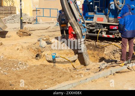 I lavoratori utilizzano un escavatore a aspirazione basato su un autocarro per campionare il terreno in un pozzo per le comunicazioni durante i lavori di restauro su strada. Foto Stock