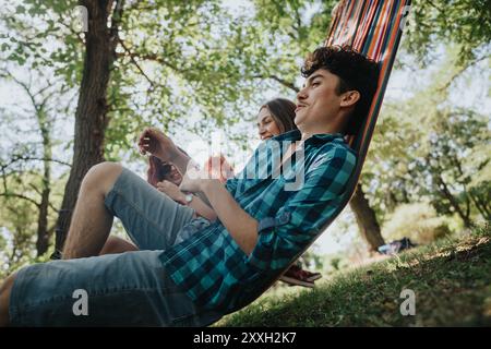 Amici che si rilassano in un'amaca godendosi una giornata di sole nel parco immerso nel verde Foto Stock