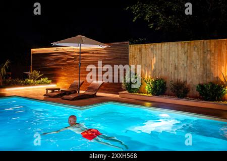 Uomo che nuota da solo nella lussuosa piscina della villa di notte Foto Stock