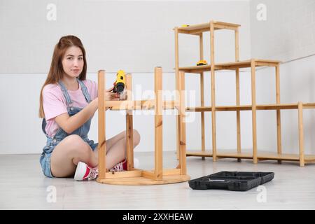 Donna con cacciavite elettrico che assembla il tavolo sul pavimento di casa Foto Stock