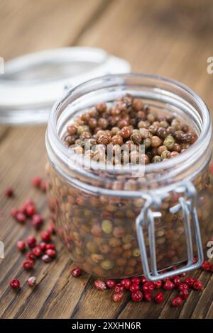 Grani di pepe rosa freschi (conservati) su un vecchio e rustico tavolo in legno, messa a fuoco selettiva, foto ravvicinata Foto Stock