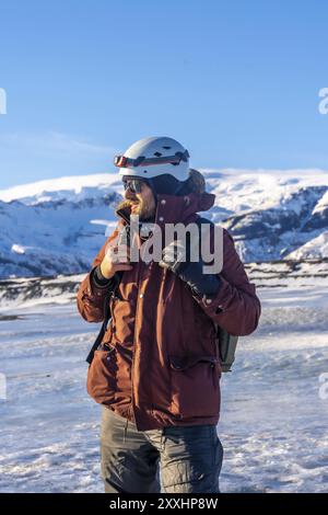 Un uomo che indossa una giacca rossa e un casco sta nella neve. Indossa uno zaino e ha un guanto nero sulla mano sinistra. Quell'uomo sta guardando in alto Foto Stock