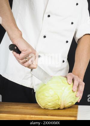 Chef professionale tenendo un affilato coltello da cucina su un cavolo cappuccio intero Foto Stock