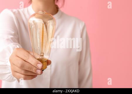 Donna che mostra una lampadina su sfondo rosa, primo piano Foto Stock