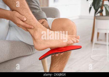 Ragazzo con i piedi piatti che si adattano alla soletta ortopedica sul divano di casa, primo piano Foto Stock