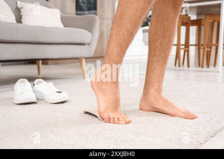 Giovane con i piedi piatti che si adattano alla soletta ortopedica a casa, primo piano Foto Stock