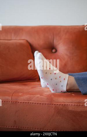 una persona si sta sdraiando su un divano con i piedi in alto e indossa calze a pois bianche Foto Stock