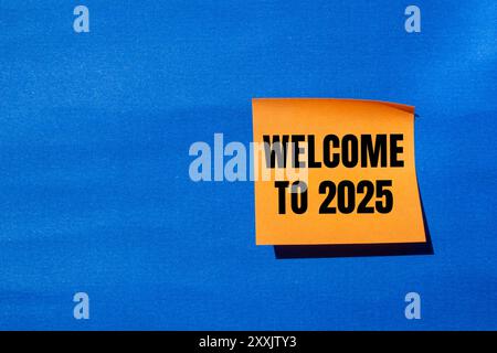 Benvenuto nel messaggio 2025 scritto su carta arancione con sfondo blu. Benvenuto concettuale nel simbolo 2025. Copia spazio. Foto Stock