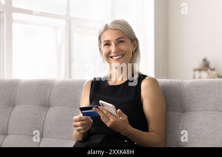 Una donna matura fa l'ordine usando carta e telefono Foto Stock