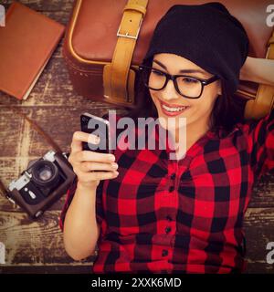 Prenditi del tempo per una pausa. Vista dall'alto di una bella giovane donna con un paio di cuffie sdraiata sul pavimento che regge il cellulare e sorride Foto Stock