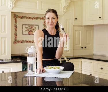 Una donna di mezza età mangia un pranzo nutriente in una cucina leggera e ariosa, come parte del suo regime alimentare sano. Spazio per le copie disponibile Foto Stock