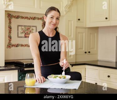 Una donna di mezza età mangia un pranzo nutriente in una cucina leggera e ariosa, come parte del suo regime alimentare sano. Spazio per le copie disponibile Foto Stock