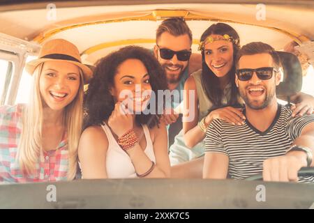 La vita è migliore quando gli amici sono vicini. Gruppo di giovani gioiosi sorridenti alla macchina fotografica mentre si siede insieme all'interno del minivan Foto Stock