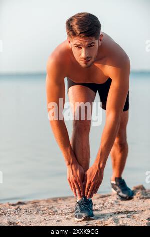 L'azione porta risultati. Giovane uomo muscoloso e sicuro di sé che si allunga correndo in piedi sulla riva del fiume Foto Stock