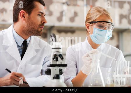 Ricerche in laboratori scientifici. Vista ad angolo basso di due giovani scienziati che fanno esperimenti mentre sono seduti in laboratorio Foto Stock