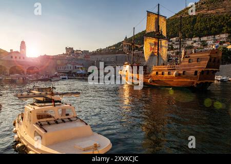 Uno sloop e piccole barche al crepuscolo nel porto di Dubrovnik, Croazia Foto Stock