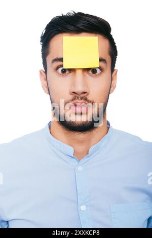 Cos'era quello? Un giovane indiano scioccato con una nota adesiva sulla fronte che ti fissa mentre ti trovi su sfondo bianco Foto Stock