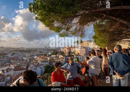 Città di Lisbona in Portogallo. Gruppi di persone si rilassano al punto panoramico di Miradouro da Graca al tramonto, con vista della capitale da una collina. Foto Stock