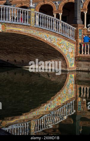 Ponte sul canale decorato con piastrelle azulejo e riflessi sull'acqua in Plaza de Espana a Siviglia, Andalusia, Spagna. Foto Stock