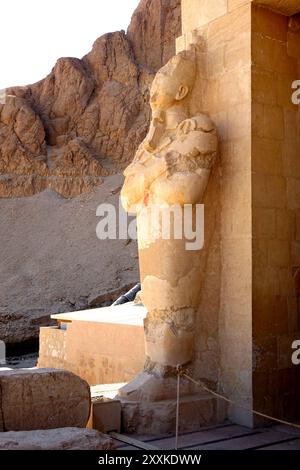 Questa antica statua si trova presso il Tempio Mortuario di Hatshepsut a Deir el Bahri, che mostra le splendide rovine architettoniche che riflettono i ri dell'Egitto Foto Stock