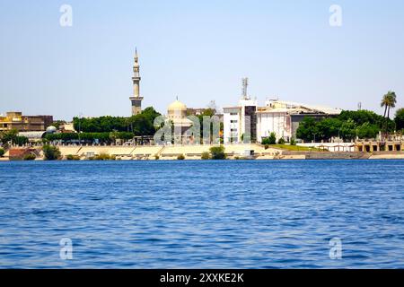 Il tranquillo fiume Nilo scorre oltre l'affascinante città di Luxor, caratterizzata da un'importante moschea e da una vegetazione lussureggiante lungo la costa, creando delle foto Foto Stock