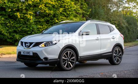 Whittlebury, Northants., Regno Unito - 25 agosto 2024: 2014 auto Nissan Qashqai bianca che guida su una strada di campagna britannica. Foto Stock