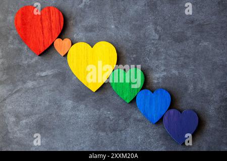 L'arcobaleno colora i cuori di legno sullo sfondo nero di pietra. Bandiera LGBT. Foto Stock