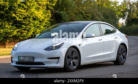 Whittlebury, Northants., Regno Unito - 25 agosto 2024: 2023 auto elettrica Tesla Model 3 bianca che guida su una strada di campagna britannica. Foto Stock