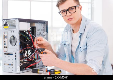 Professionale intelligente. Ritratto di un bel giovane che ripara il computer seduto al suo posto di lavoro Foto Stock