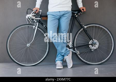 Uomo con la bicicletta. Primo piano di un uomo che si appoggia alla sua bicicletta mentre è in piedi su uno sfondo grigio Foto Stock