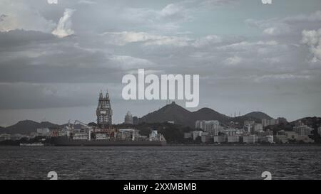 Un colpo basso di una grande piattaforma petrolifera offshore ancorata vicino alla costa di Niteroi, in Brasile, con gli edifici della città e le verdi colline sullo sfondo unde Foto Stock