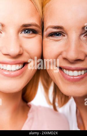 Figlia con madre. Primo piano della madre e della figlia sorridono e guardano la fotocamera mentre si alzano dalla guancia alla guancia su sfondo bianco Foto Stock