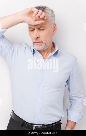 Si sente esausto. Uomo anziano stanco in camicia che tocca la testa con la mano e tiene gli occhi chiusi mentre si sta in piedi su sfondo bianco Foto Stock