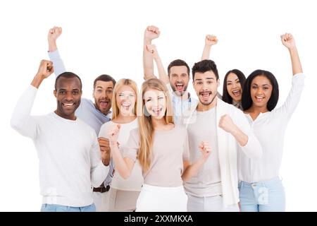 Squadra di successo. Gruppo di giovani felici in abbigliamento casual elegante che guardano la macchina fotografica e tengono le braccia sollevate mentre sono in piedi su sfondo bianco Foto Stock