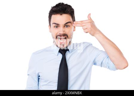 Giornata troppo stressante. Giovane frustrato in camicia e cravatta che gestiva pistola vicino alla testa e tiene la bocca aperta mentre si trova contro il backgroun bianco Foto Stock