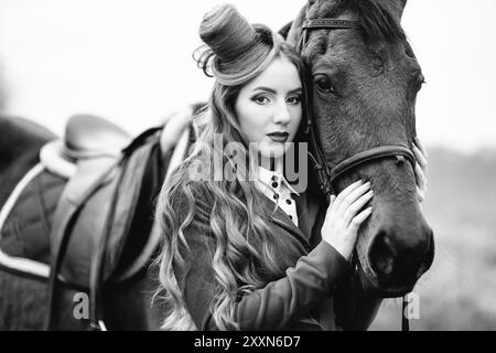 ragazza di fantino dai capelli rossi in un cardigan rosso e stivali neri alti con un cavallo per una passeggiata Foto Stock