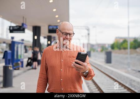 Senior finlandese che utilizza il telefono cellulare alla stazione ferroviaria Foto Stock