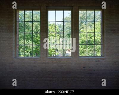 Tre finestre a vetro singolo in un muro di mattoni a vista in un vecchio impianto industriale. Foto Stock