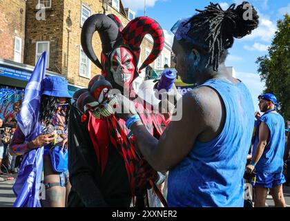 Londra, Regno Unito, 25 agosto 2024. I partecipanti al gruppo "Blue Dutty Mas" saranno coperti da polveri di vernice brillante e celebreranno alcuni dei simbolismi e personaggi mas (mascherate) di J'Ouvert, parte del carnevale caraibico, specialmente a Trinidad. La solita domenica mattina J'Ouvert fu cancellata, ma i festeggiamenti continuarono più tardi. La domenica del Carnevale di Notting Hill è iniziata con il tradizionale Carnevale dei bambini di oggi e più tardi ha visto i festeggiamenti festeggiare il fine settimana festivo partecipando o guardando lungo il percorso del carnevale, presso sistemi sonori, bancarelle e locali. Foto Stock