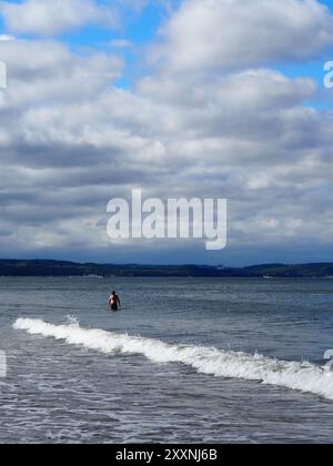 Danzica, Polonia - 13 luglio 2024: Una persona si alza al ginocchio nell'oceano mentre guarda l'orizzonte, sotto il cielo pieno di spesse nuvole, catturando un m Foto Stock