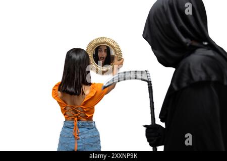 Spaventata giovane donna, vista da dietro e riflessa in uno specchio, si confronta con il triste mietitore, vestito con un costume di Halloween con un mantello scuro, Foto Stock