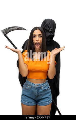 Vertical Grim reaper, vestito con un costume di Halloween con un mantello scuro e un volto scheletrico, tiene minacciosamente una falce mentre minaccia un giovane terrorizzato Foto Stock