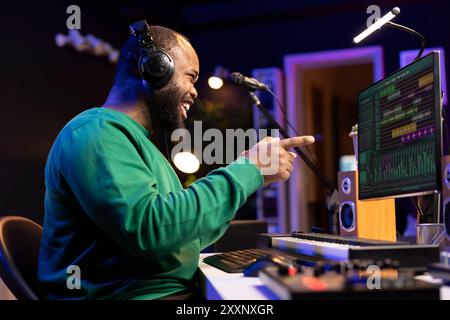 L'artista cantautore si sente soddisfatto dei suoi file audio registrati in studio domestico, lavorando con la console di mixaggio per comporre nuova musica. Un ingegnere del suono che produce brani creativi su software. Foto Stock