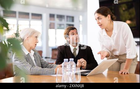 tre lavoratori d'ufficio positivi sono seduti al tavolo animatamente e attivamente per discutere il lavoro in corso Foto Stock